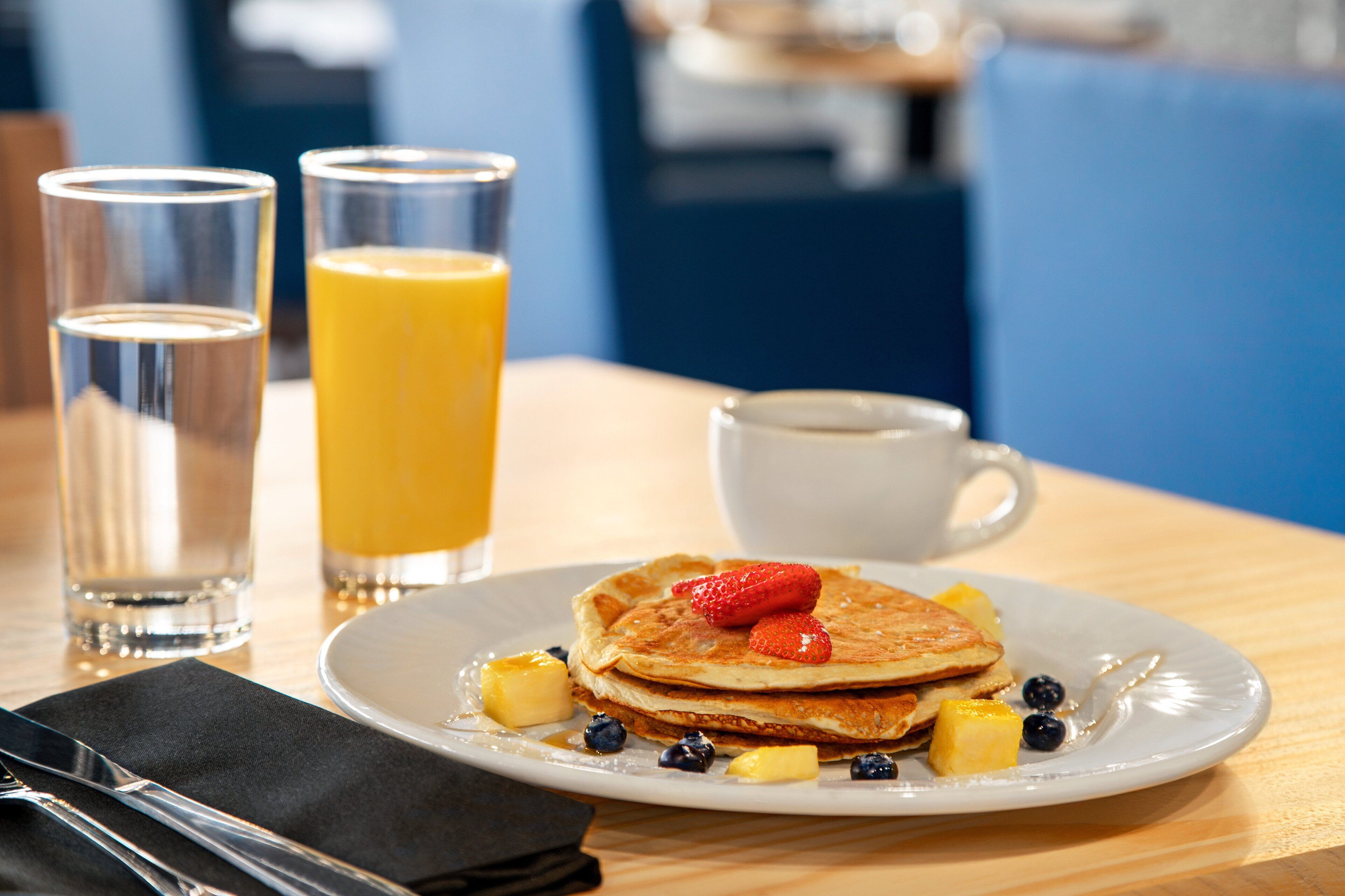 A breakfast setting with pancakes, blueberries, and a glass of orange juice on a plate.