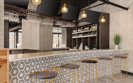 A bar area with hexagonal patterned walls, a counter with stools, and hanging light fixtures.