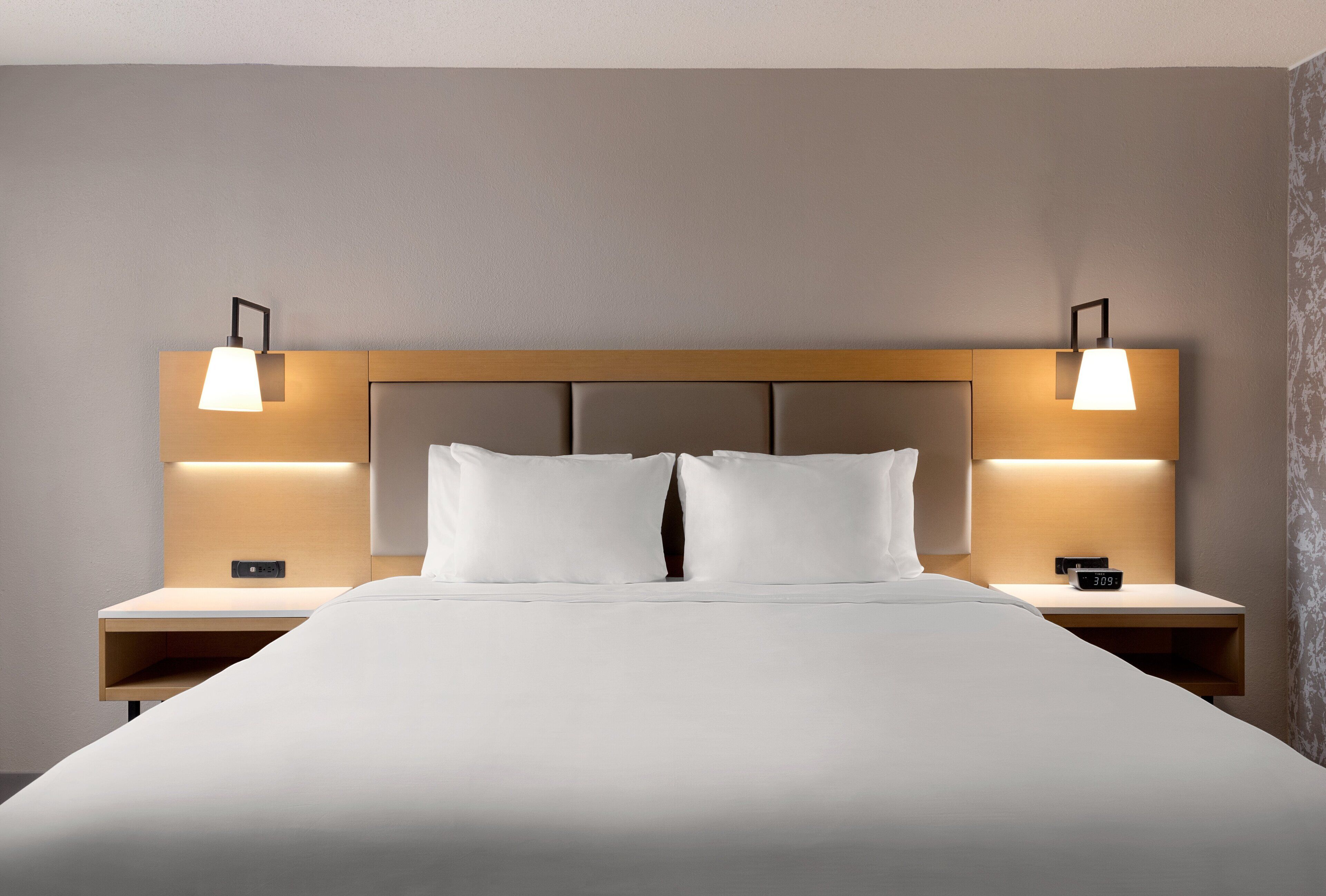 Une chambre d’hôtel avec un grand lit, deux tables de chevet et deux lampes fixées au mur.