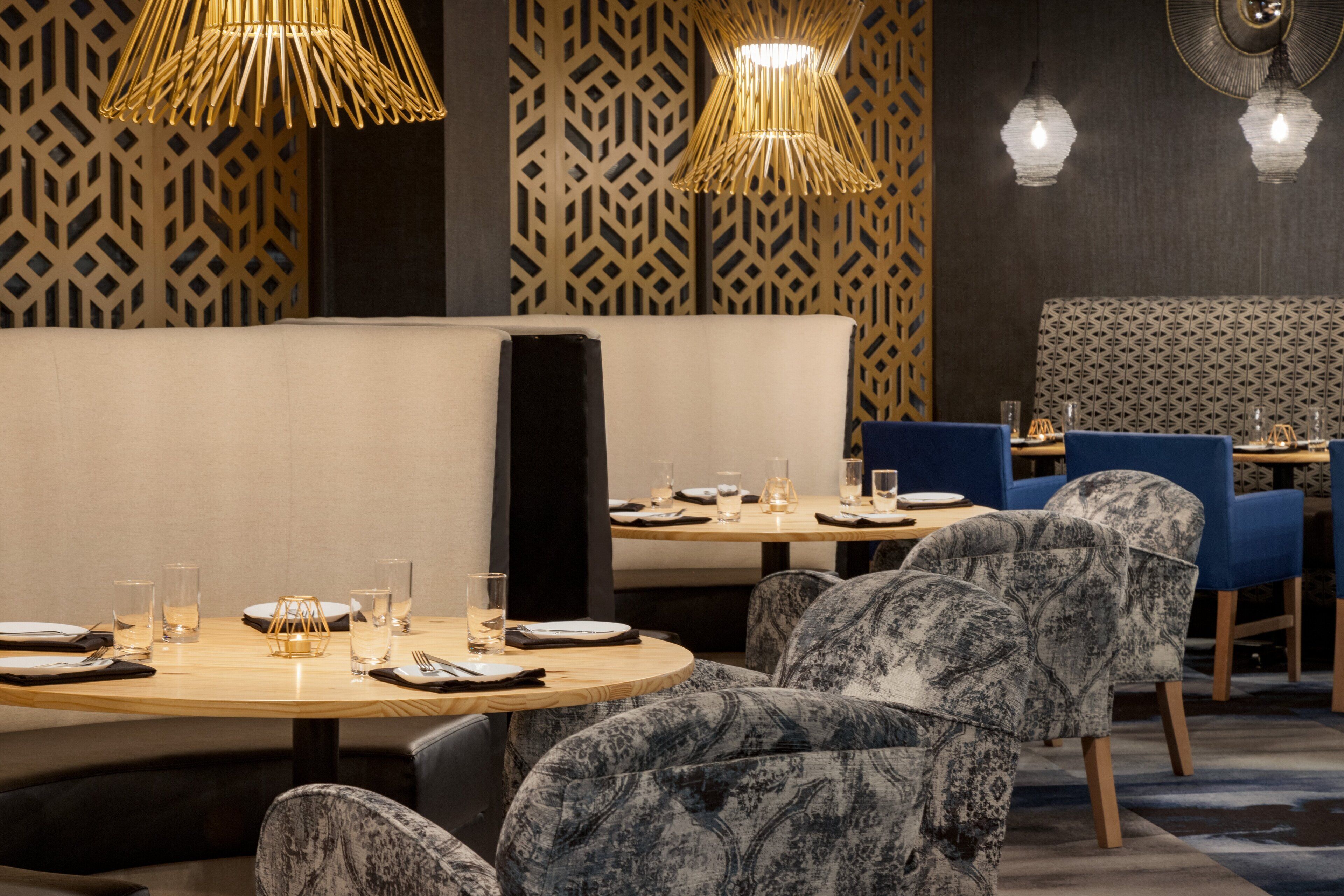 A restaurant with a modern interior, featuring patterned walls, round tables, and upholstered chairs.