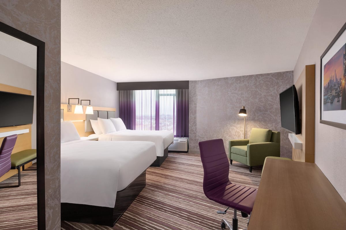 A hotel room with two beds, a desk, a chair, a TV, and a window with curtains.