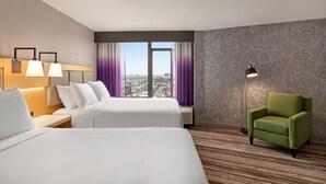 A hotel room with two beds, a green armchair, a large window with purple curtains, and a floor lamp.