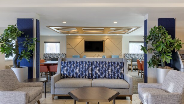 A modern hotel lobby with a sofa, armchairs, a coffee table, and potted plants. - Holiday Inn Express San Bernardino - Colton by IHG (Colton)