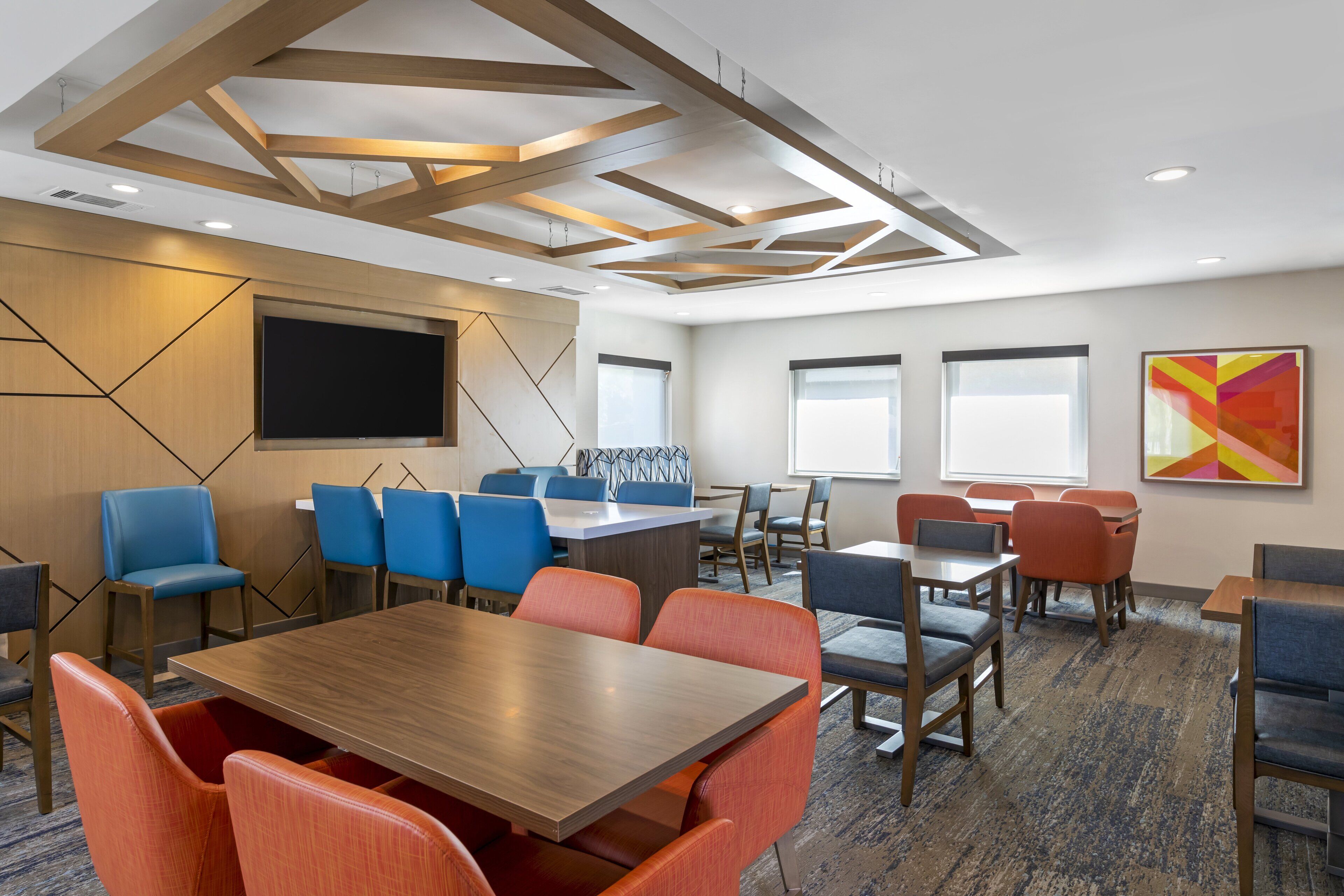 A conference room with a large table, blue and orange chairs, a flat-screen TV, and a modern ceiling design.
