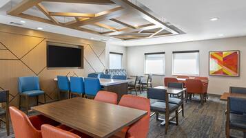 A conference room with a large table, blue and orange chairs, a flat-screen TV, and a modern ceiling design.