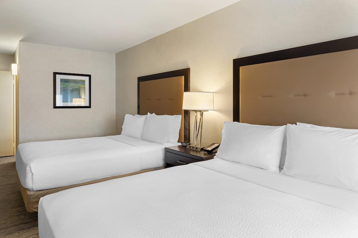 A hotel room with two beds, a nightstand with a lamp, and a framed picture on the wall.
