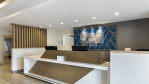 A modern reception desk with a wooden accent, a blue geometric wall design, and a sign indicating the hotel name. - Holiday Inn Express San Bernardino - Colton by IHG (Colton)