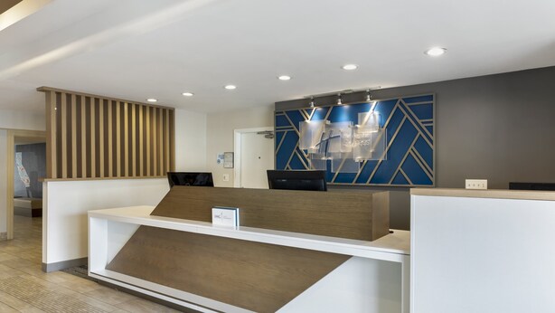 A modern reception desk with a wooden accent, a blue geometric wall design, and a sign indicating the hotel name. - Holiday Inn Express San Bernardino - Colton by IHG (Colton)