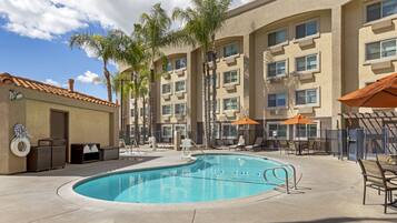 Relax by the clear pool surrounded by lounge chairs and umbrellas, with palm trees adding to the tropical ambiance.