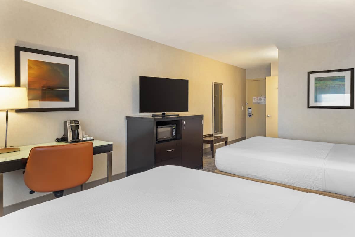 A hotel room with two beds, a desk with a coffee maker, a TV, and framed artwork on the walls.