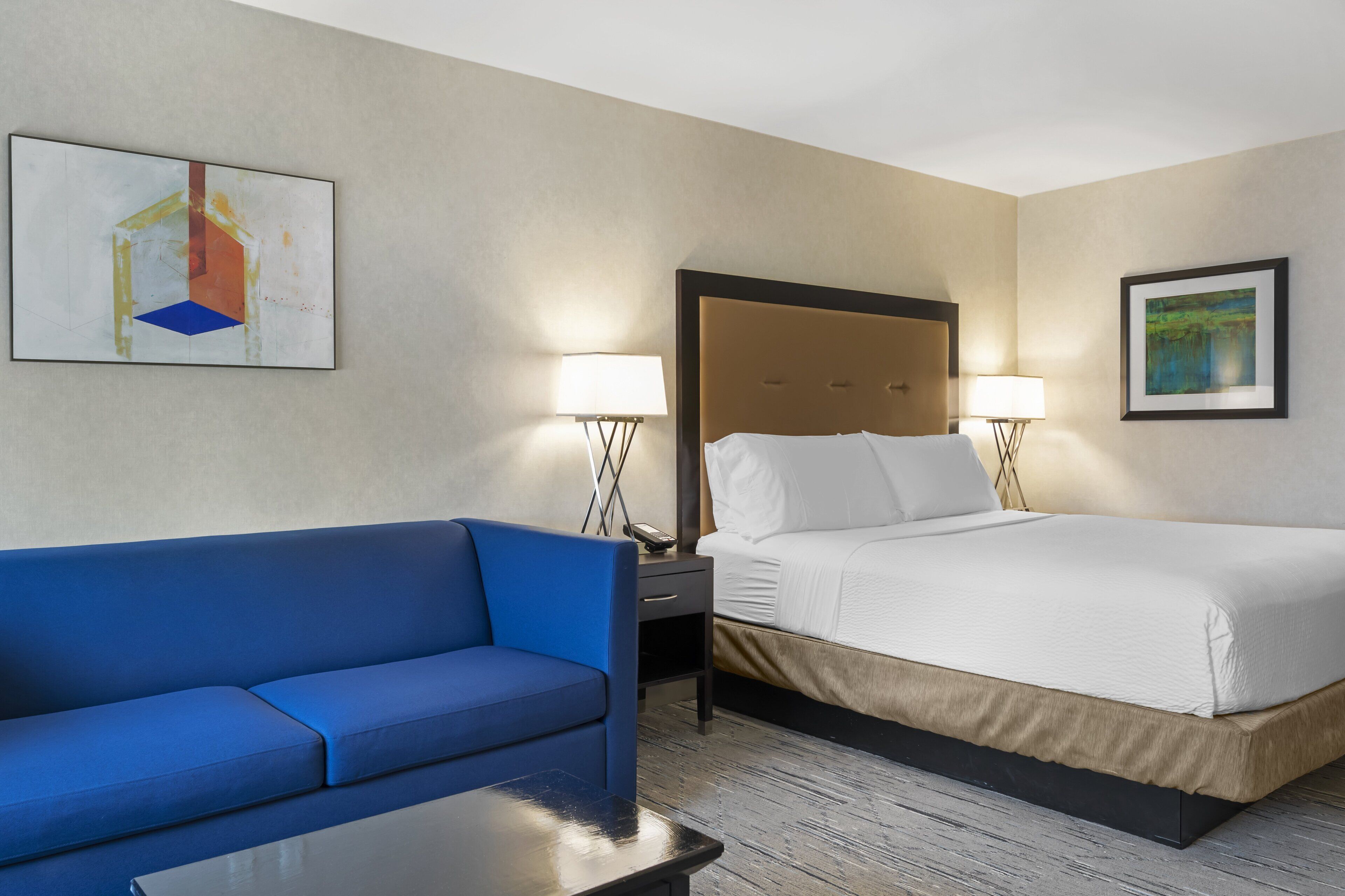 Une chambre d’hôtel avec un lit, un canapé bleu, une petite table et deux lampes de chevet.