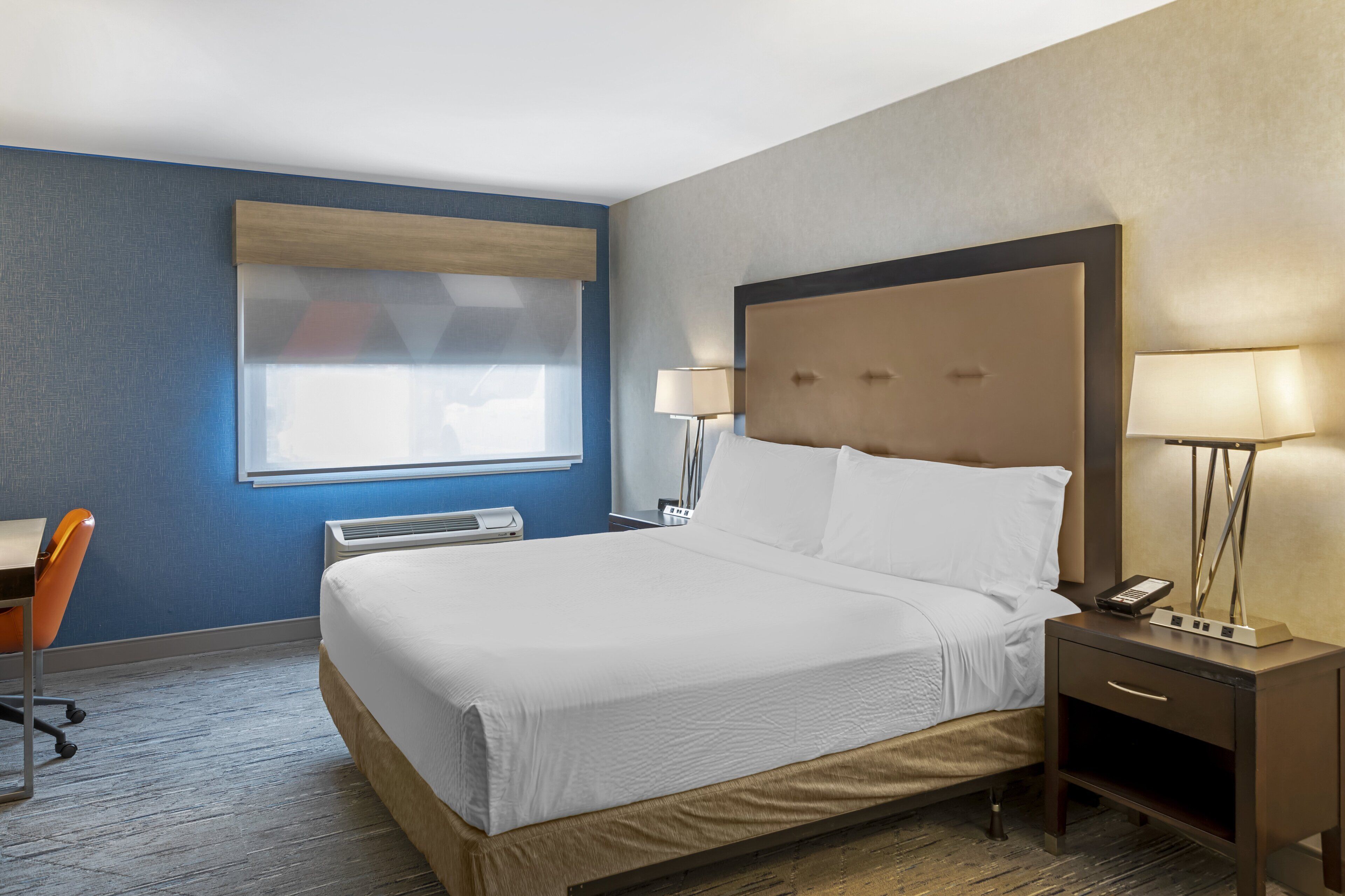 Ein Hotelzimmer mit einem großen Bett, einem Schreibtisch, einer Klimaanlage und einem Fenster mit Jalousien.