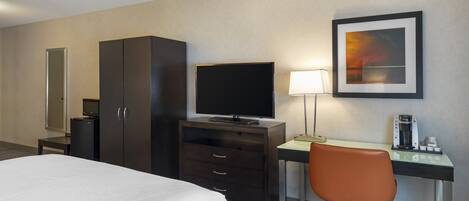 A hotel room with a bed, a desk with a chair, a television, a coffee maker, and a framed picture on the wall.