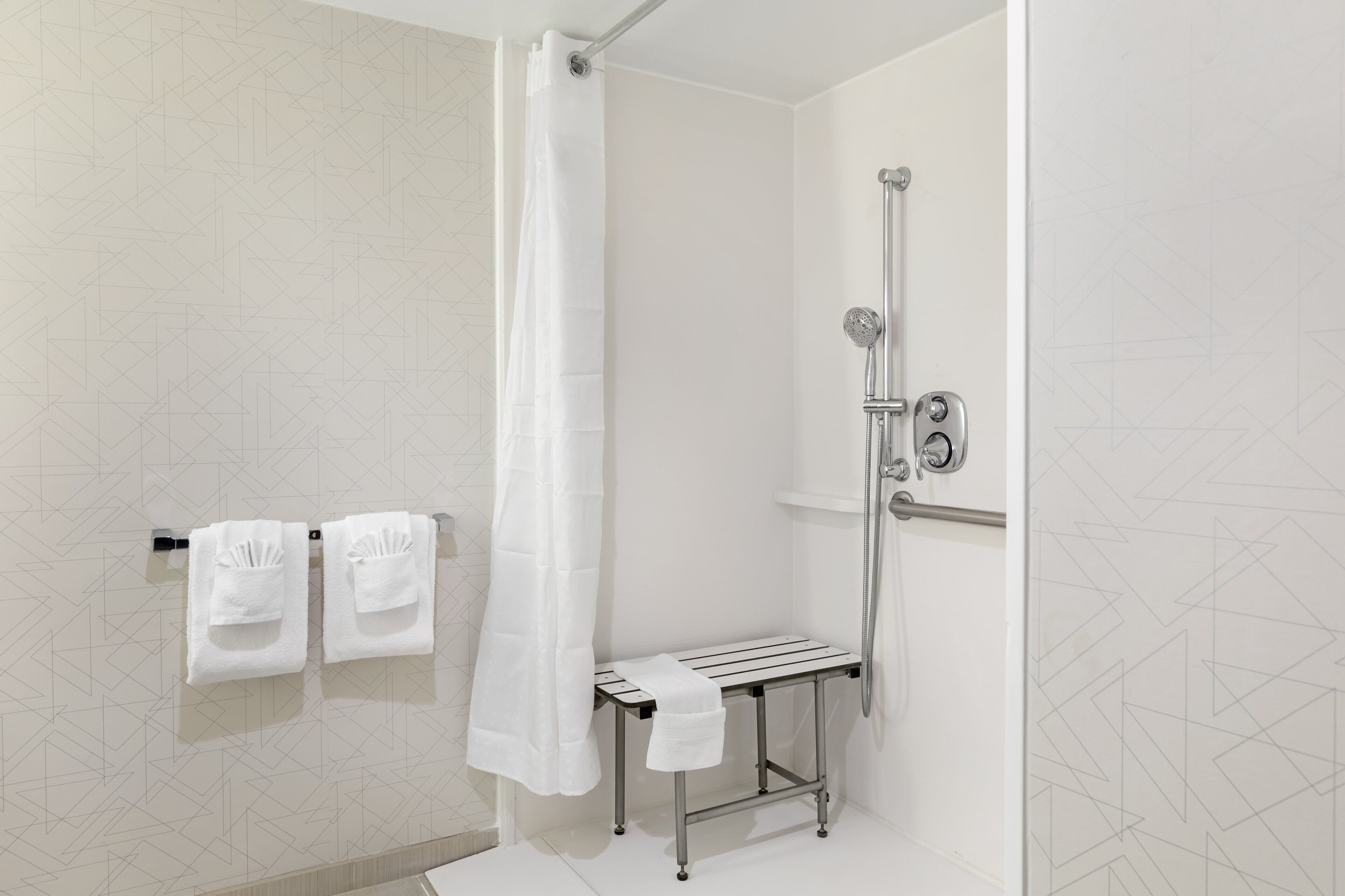 Une salle de bain moderne équipée d’une douche, d’un porte-serviettes avec deux serviettes et d’un banc.
