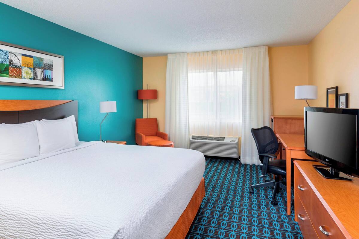 A hotel room with a large bed, a desk with a TV, a chair, and a window with curtains.