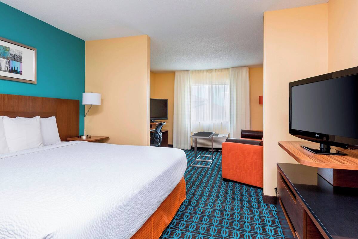 A hotel room with a large bed, a TV, a desk, and a chair.