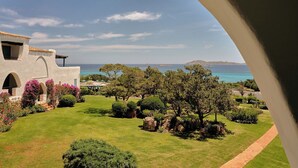 A coastal view through an archway, featuring a well-maintained garden, a building with a tiled roof, and a clear view of the sea and distant land. - Romazzino, A Belmond Hotel, Costa Smeralda (Arzachena)
