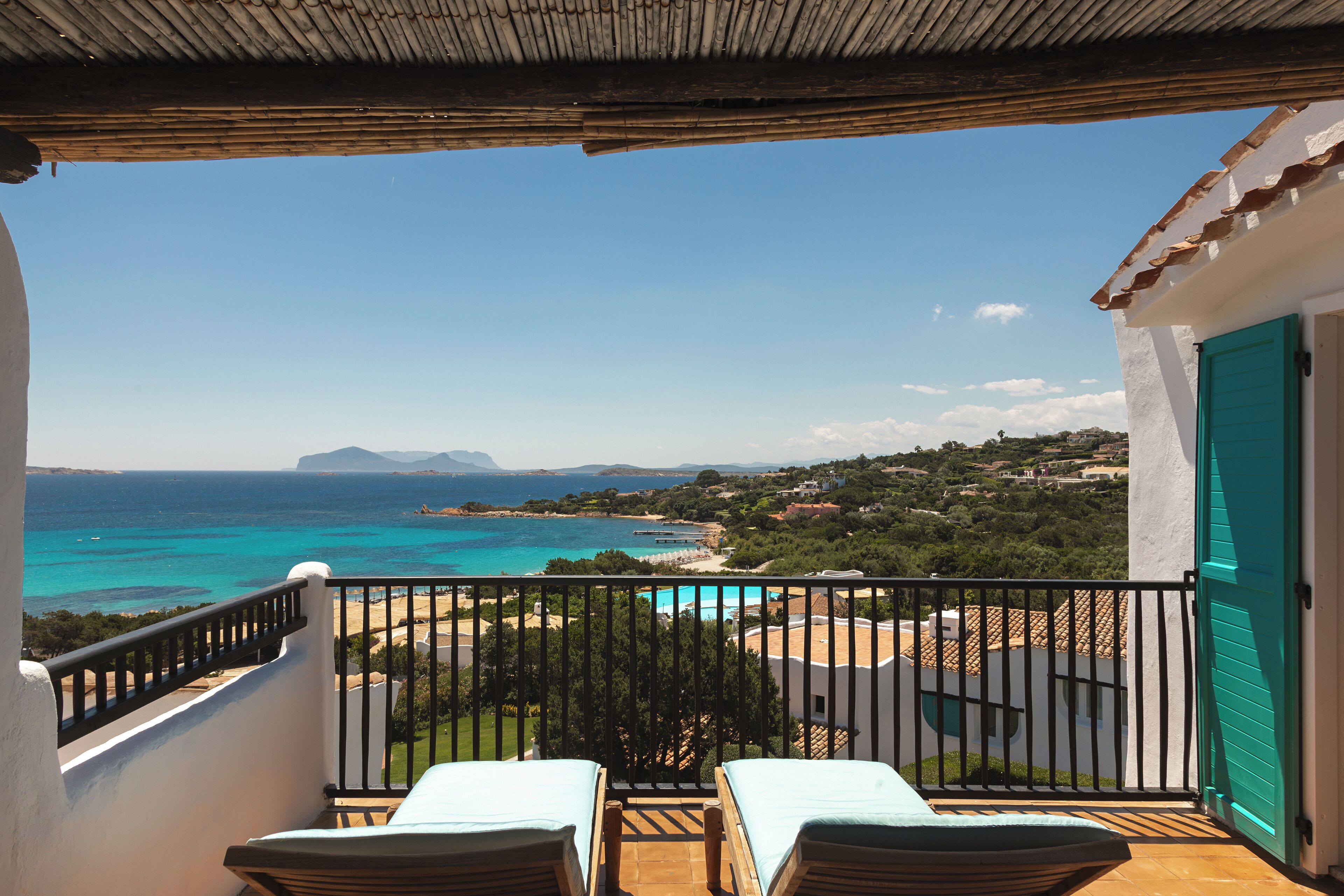 Un balcon avec deux fauteuils, une vue sur la mer et une porte turquoise.