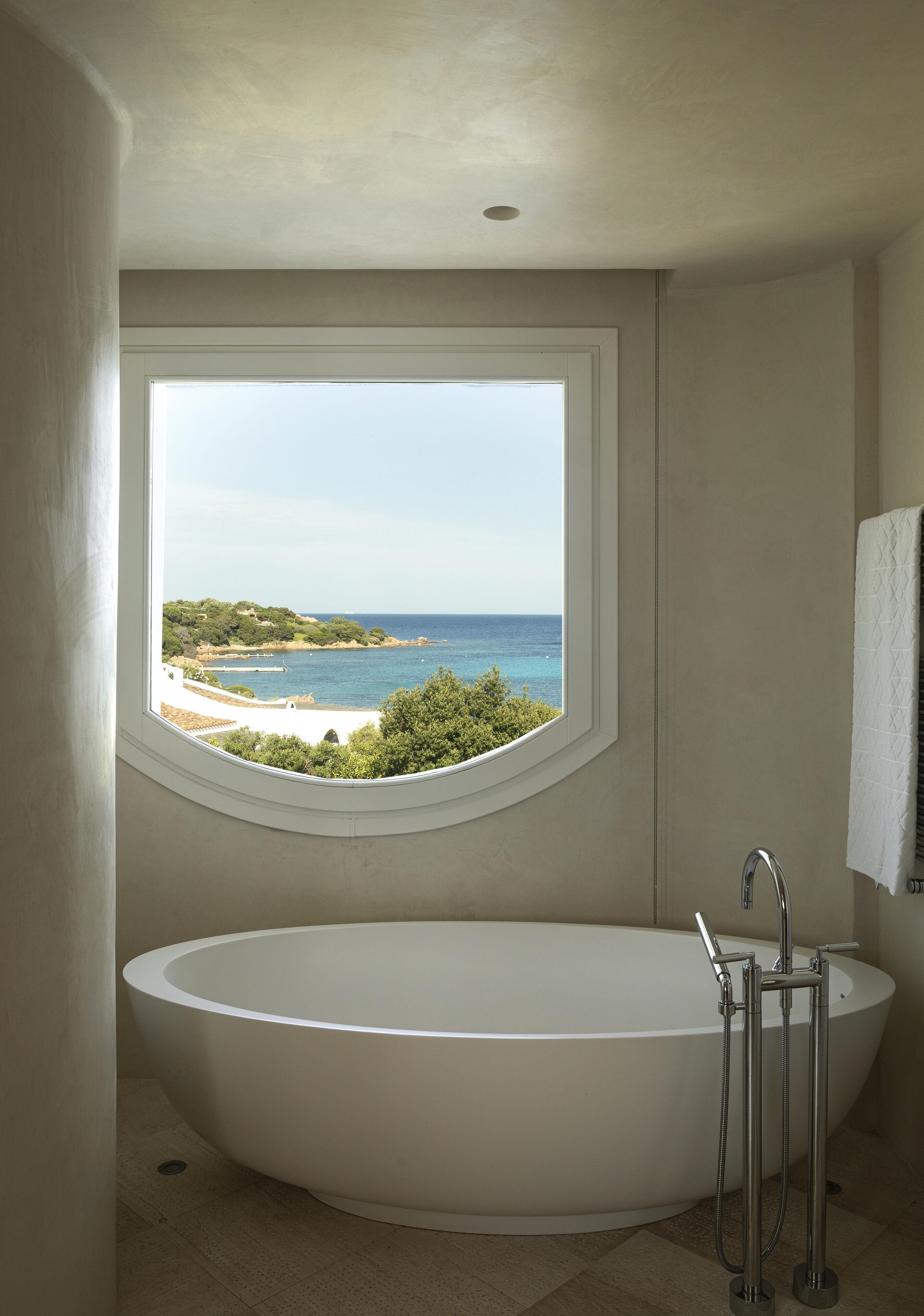 Un baño con una bañera grande, una ventana con vista a una playa y una toalla colgada en la pared.