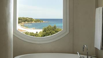 Un baño con una bañera grande, una ventana con vista a una playa y una toalla colgada en la pared.