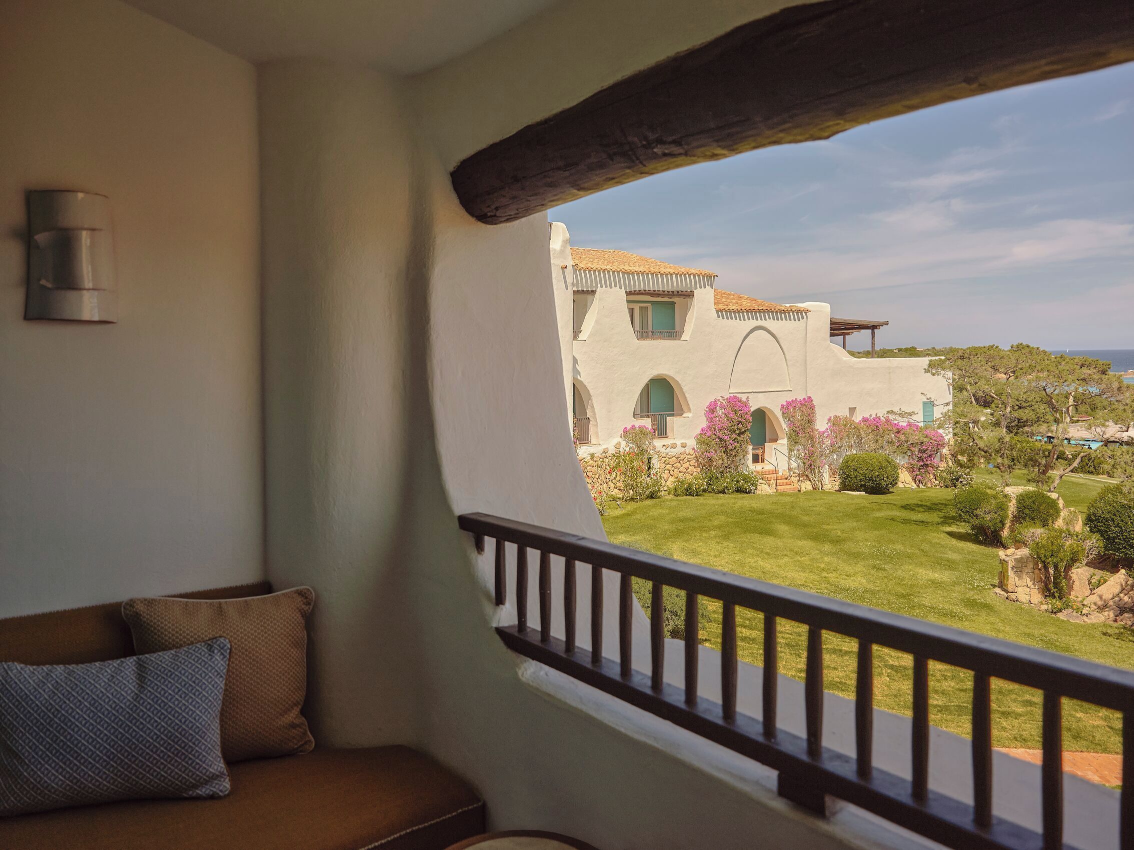A balcony with a view of a white building with arches and a garden.
