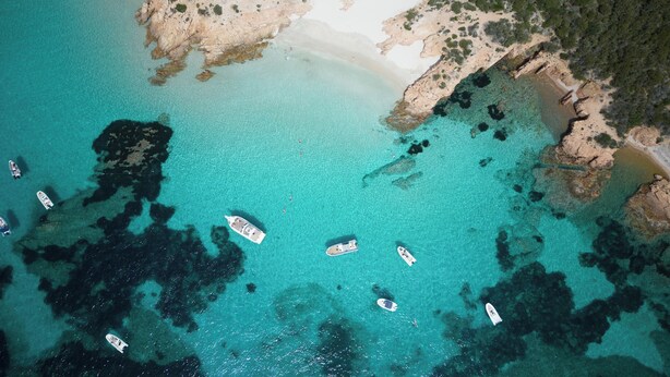 An aerial view of a coastal area with clear turquoise waters, rocky outcrops, and several boats anchored near the shore. - Romazzino, A Belmond Hotel, Costa Smeralda (Arzachena)