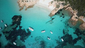 An aerial view of a coastal area with clear turquoise waters, rocky outcrops, and several boats anchored near the shore. - Romazzino, A Belmond Hotel, Costa Smeralda (Arzachena)