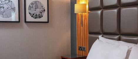 A hotel room with a large bed, a nightstand with a lamp, and two framed artworks on the wall.