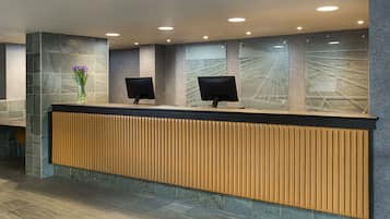 Un mostrador de recepción con dos monitores, un florero con flores y un diseño moderno con detalles de piedra y madera.