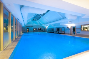 Una piscina interior con suelo azul, techo de diseño geométrico y pared de vidrio en un lateral.