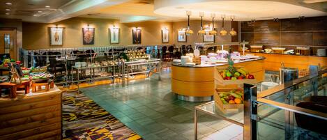 A hotel lobby with a central fruit display, seating areas, and a reception desk.