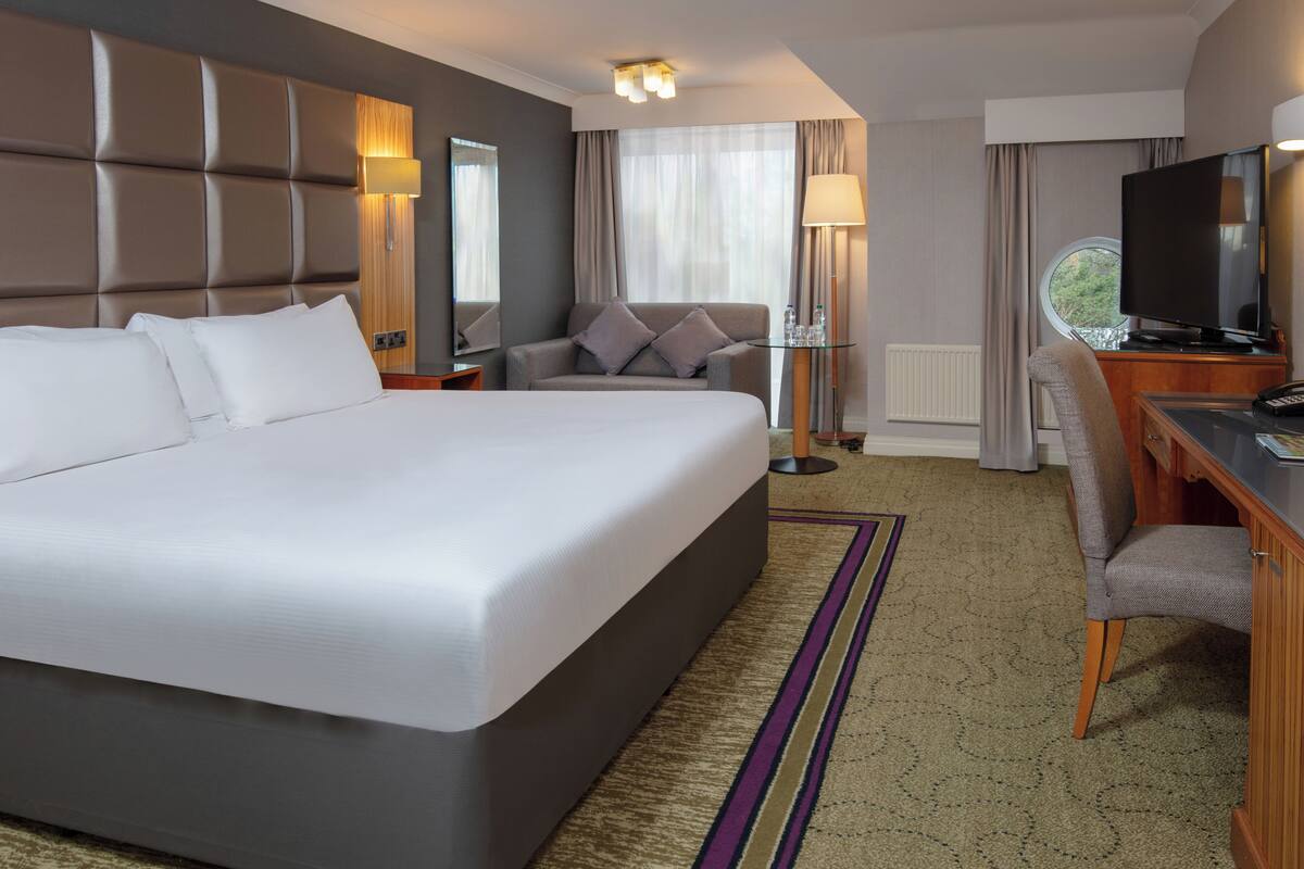 A hotel room with a large bed, a desk with a TV, a sofa, and a lamp.