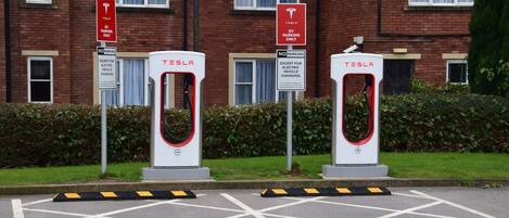 Two Tesla electric vehicle charging stations in front of a brick building with windows and a lamp post.