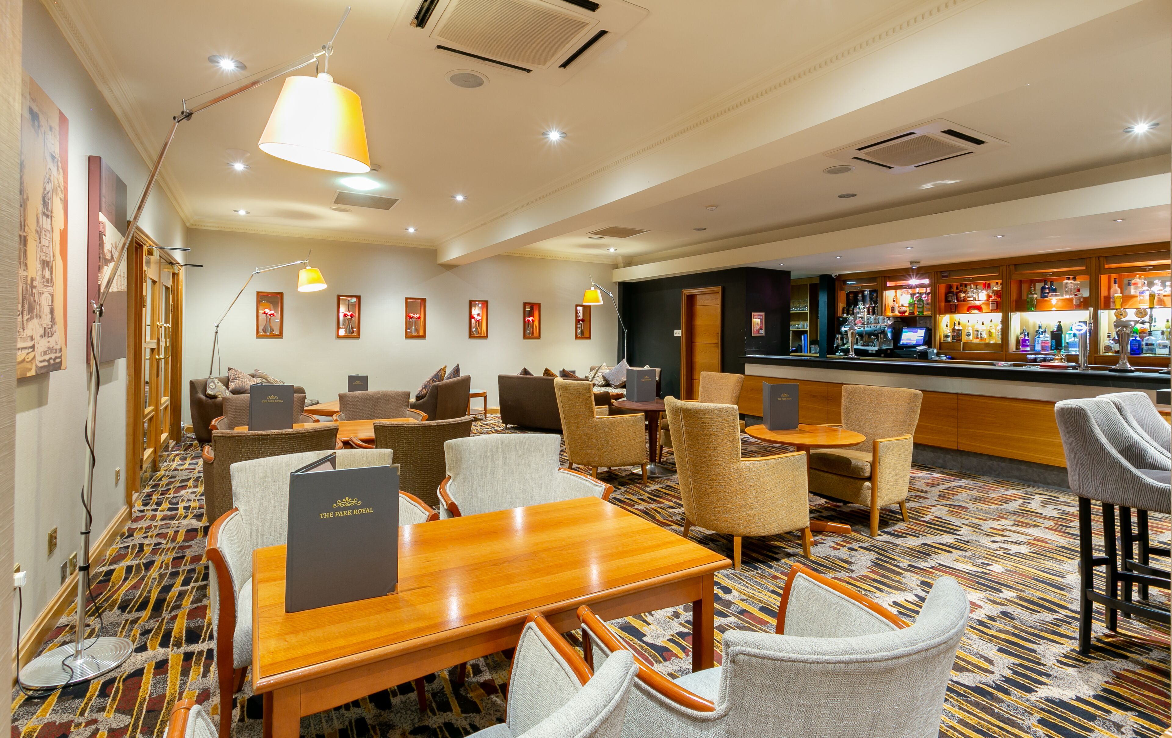 A hotel lobby with a bar area, seating arrangements, and a patterned carpet.