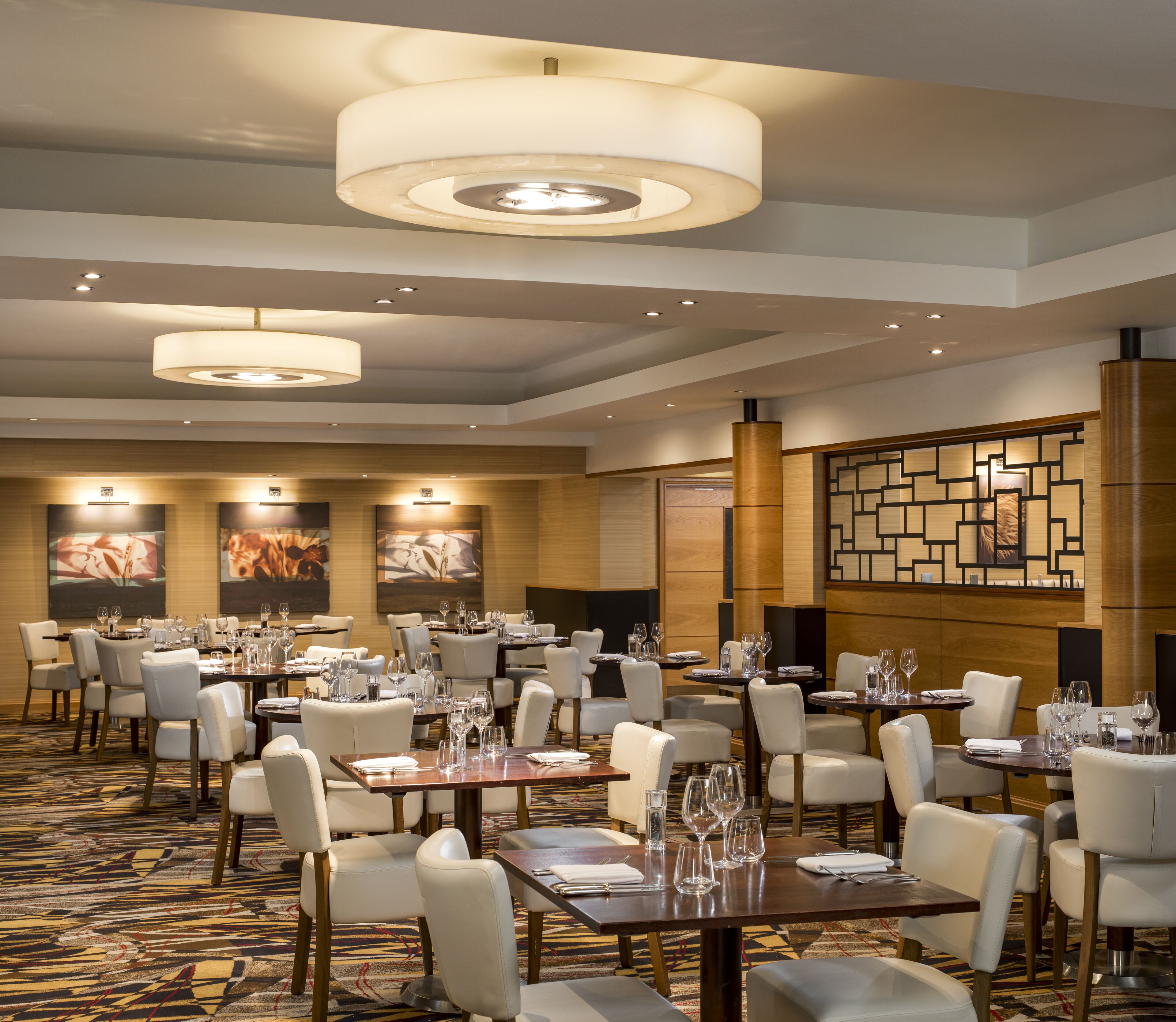 A hotel dining area with multiple tables set for dining, chairs, and overhead lighting.