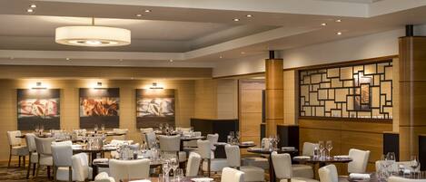 A hotel dining area with multiple tables set for dining, chairs, and overhead lighting.