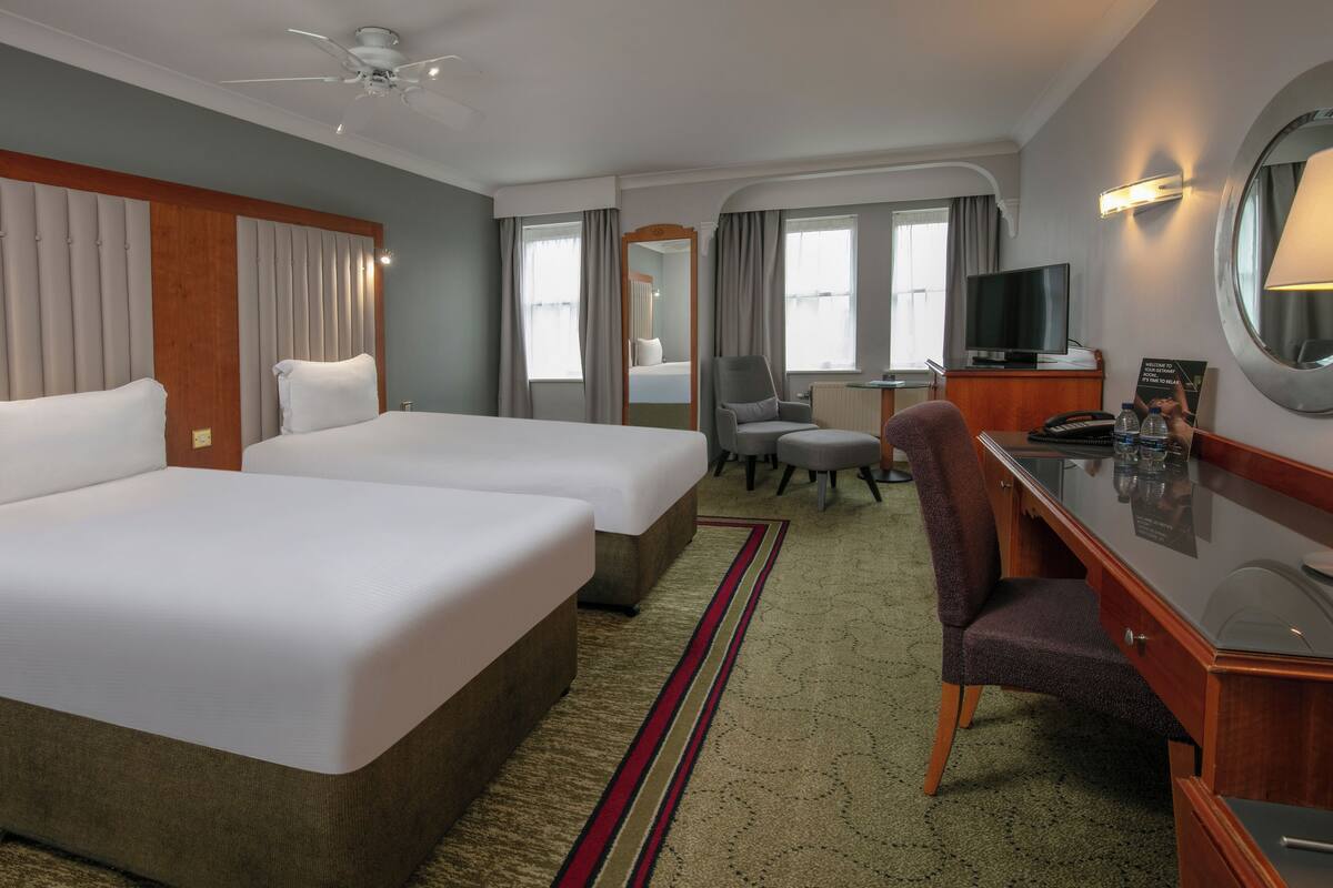 A hotel room with two beds, a desk, a chair, a television, and a mirror.