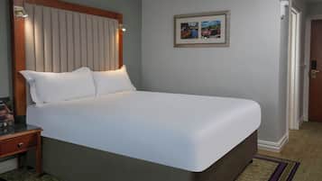 A neatly made bed in a hotel room with a wooden headboard, a framed picture on the wall, and a door to the right.