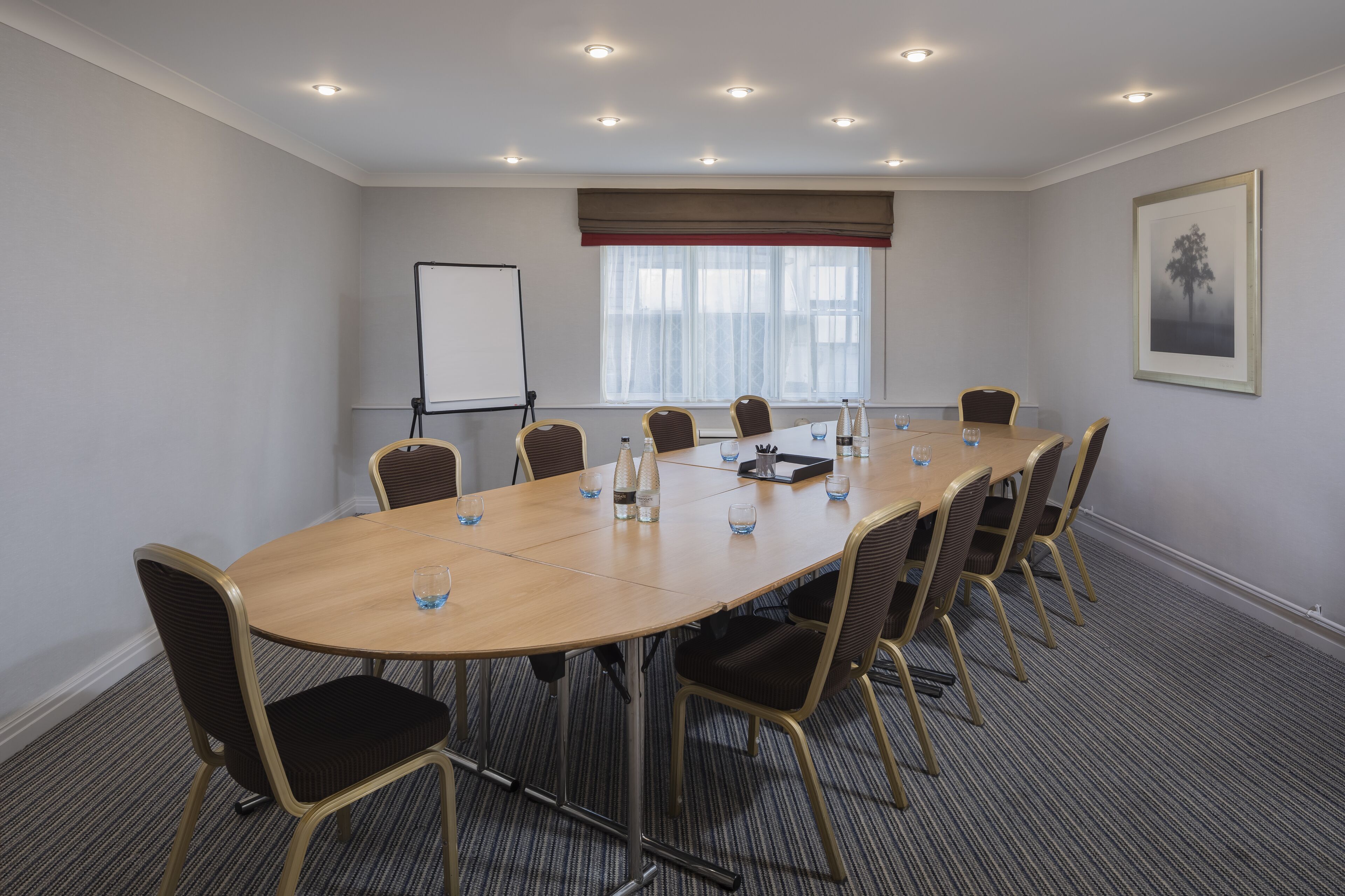 A conference room with a long table, chairs, a whiteboard, and a window with blinds.