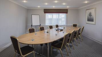 A conference room with a long table, chairs, a whiteboard, and a window with blinds.