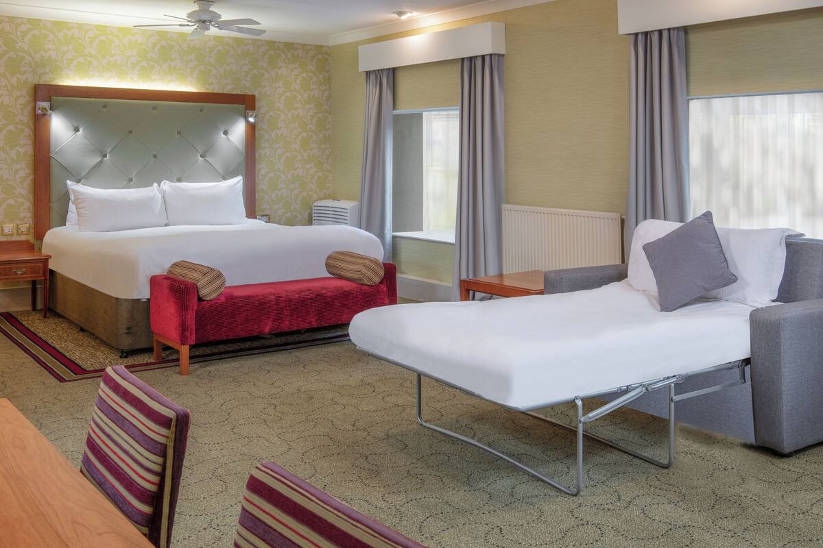 A hotel room with a large bed, a sofa, a small table, and a chair.