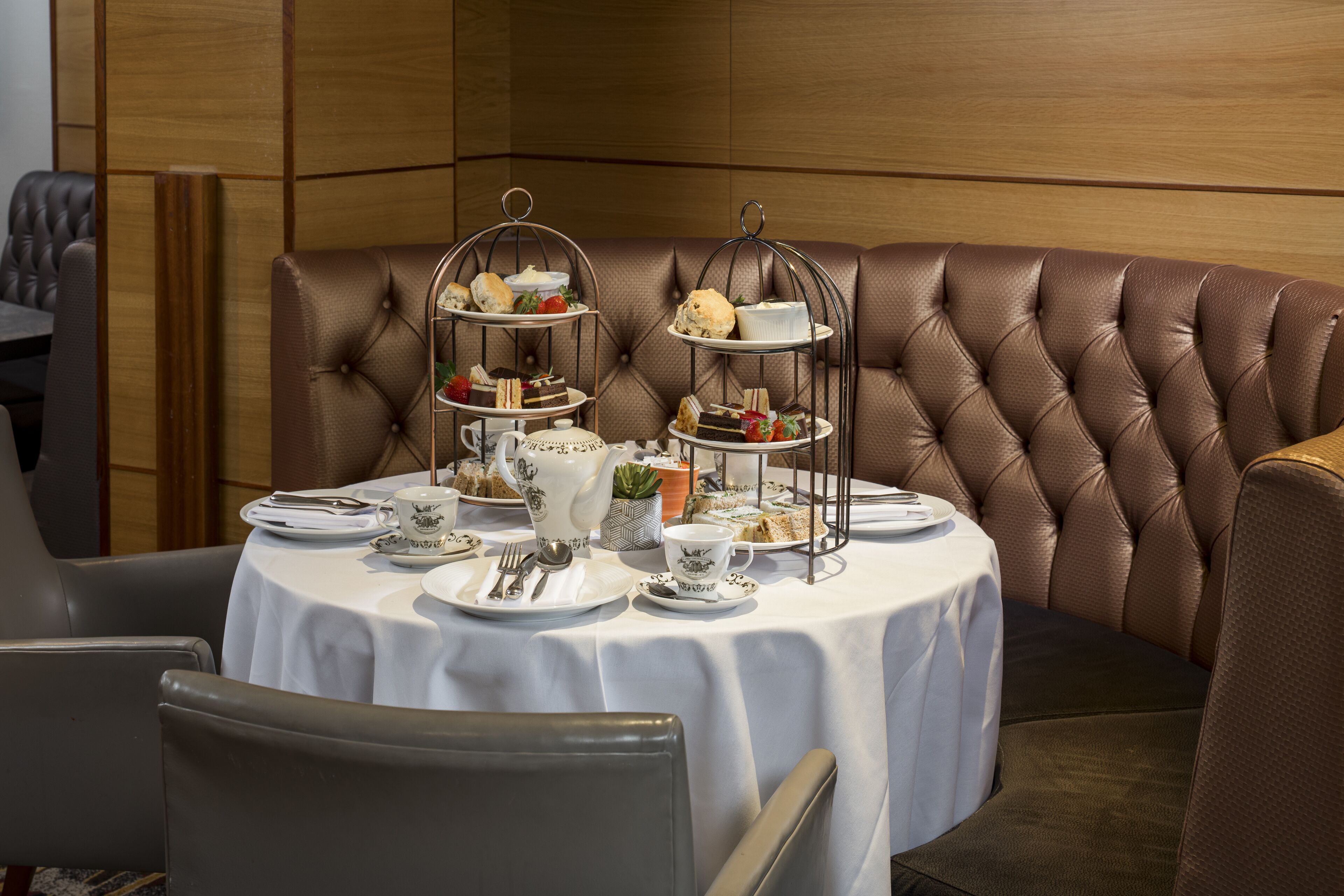 Un coin repas avec une table ronde dressée pour un service à thé, agrémentée d’un présentoir à étages et d’une variété de pâtisseries et de sandwichs.