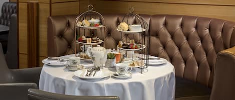 A dining area with a round table set for a tea service, complete with tiered tea stands and a variety of pastries and sandwiches.