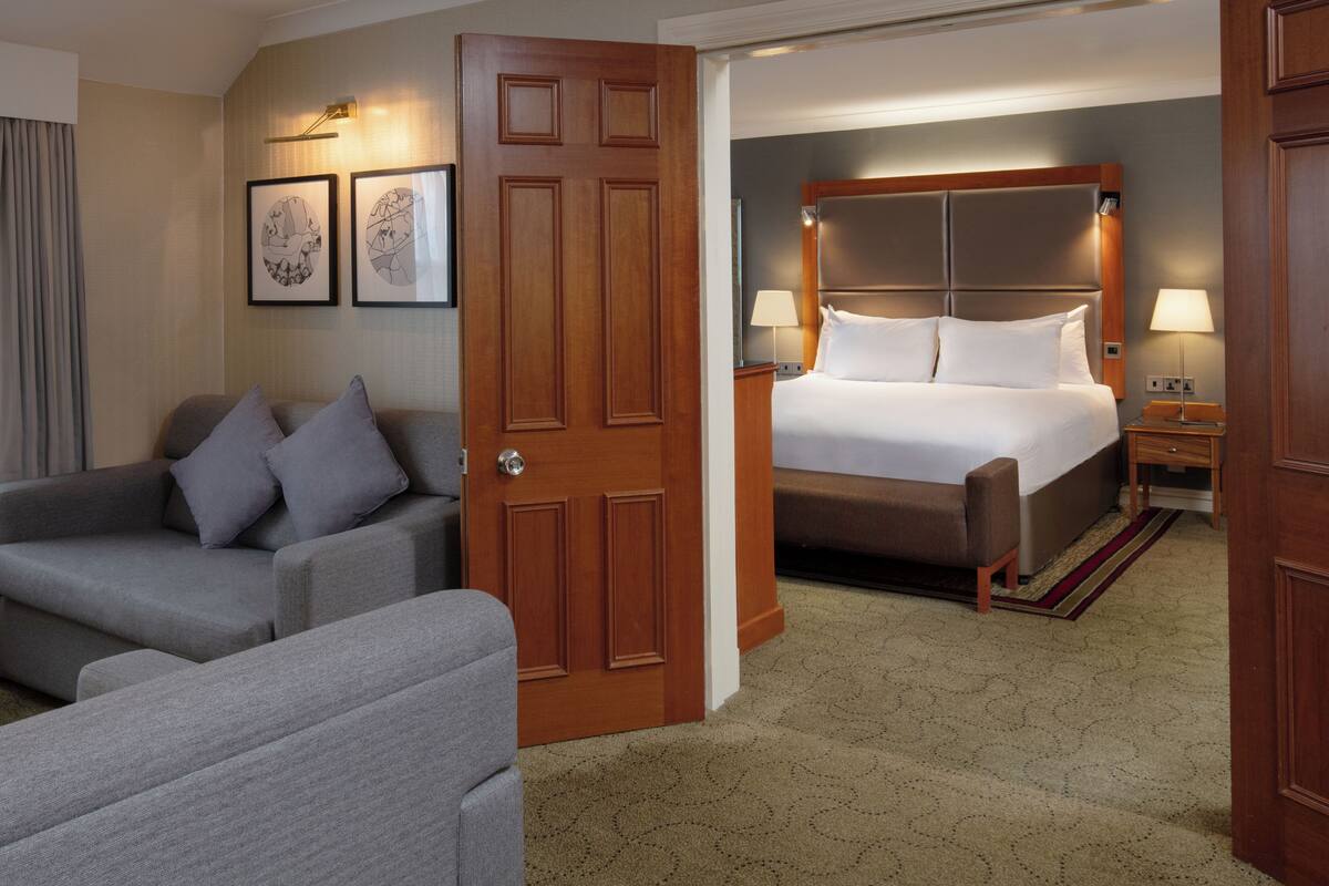 A hotel room with a bed, two bedside tables, a sofa, and a door.
