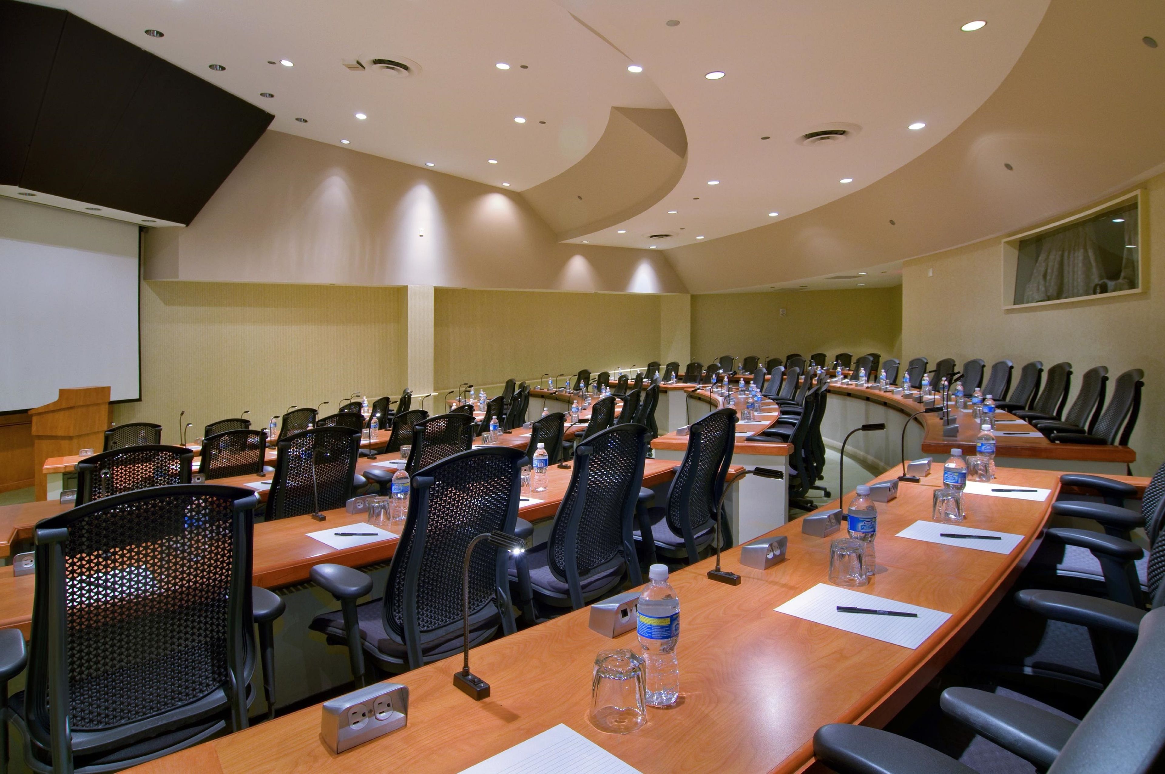 A conference room with long tables, chairs, water bottles, and a projector screen.
