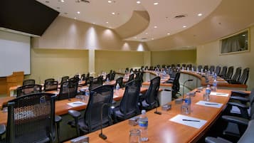 A conference room with long tables, chairs, water bottles, and a projector screen.