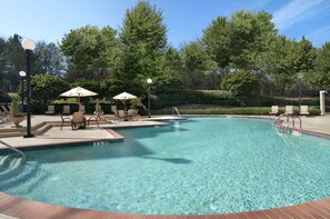 A clear swimming pool with lounge chairs and umbrellas, surrounded by trees and a fence. - Hilton Atlanta Airport (Atlanta)