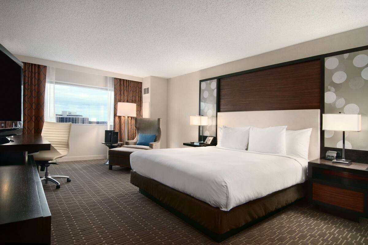 Habitación de hotel con una cama grande, dos mesitas de noche, un escritorio, una silla y una ventana con cortinas.