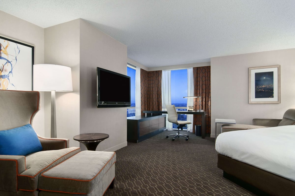 Una habitación de hotel con una cama grande, un escritorio con computadora, una silla, un televisor y una ventana con vista a la ciudad.