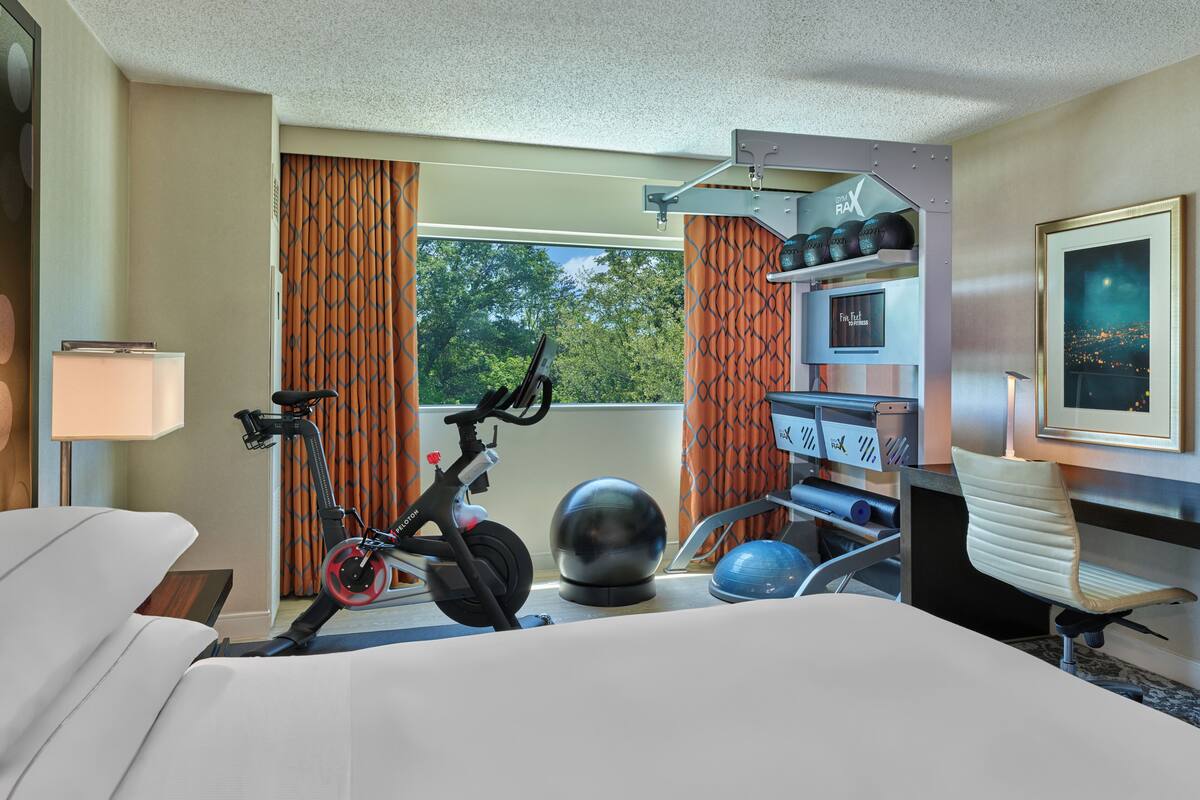 Habitación de hotel con cama, bicicleta estática, pelota de ejercicios y escritorio con silla.